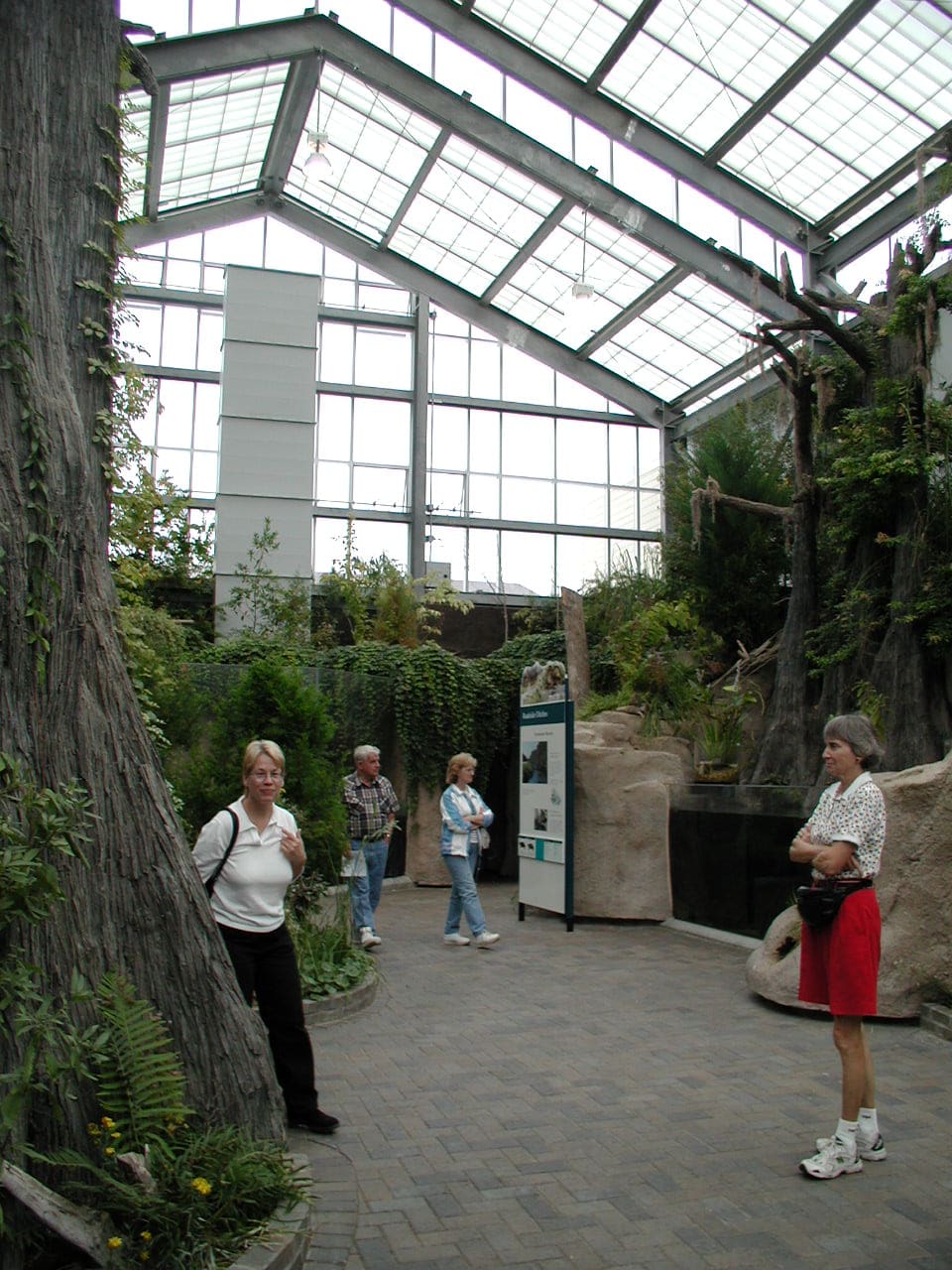 Visitors walking past the glass and timber aquarium building among tall pines