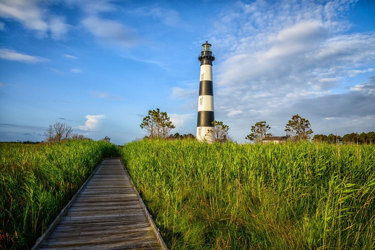 A wooden boardwalk running out through tall marsh grass toward the lighthouse