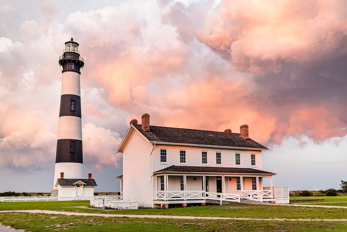 The black and white banded tower and the white keepers' quarters under pink sunrise cloud