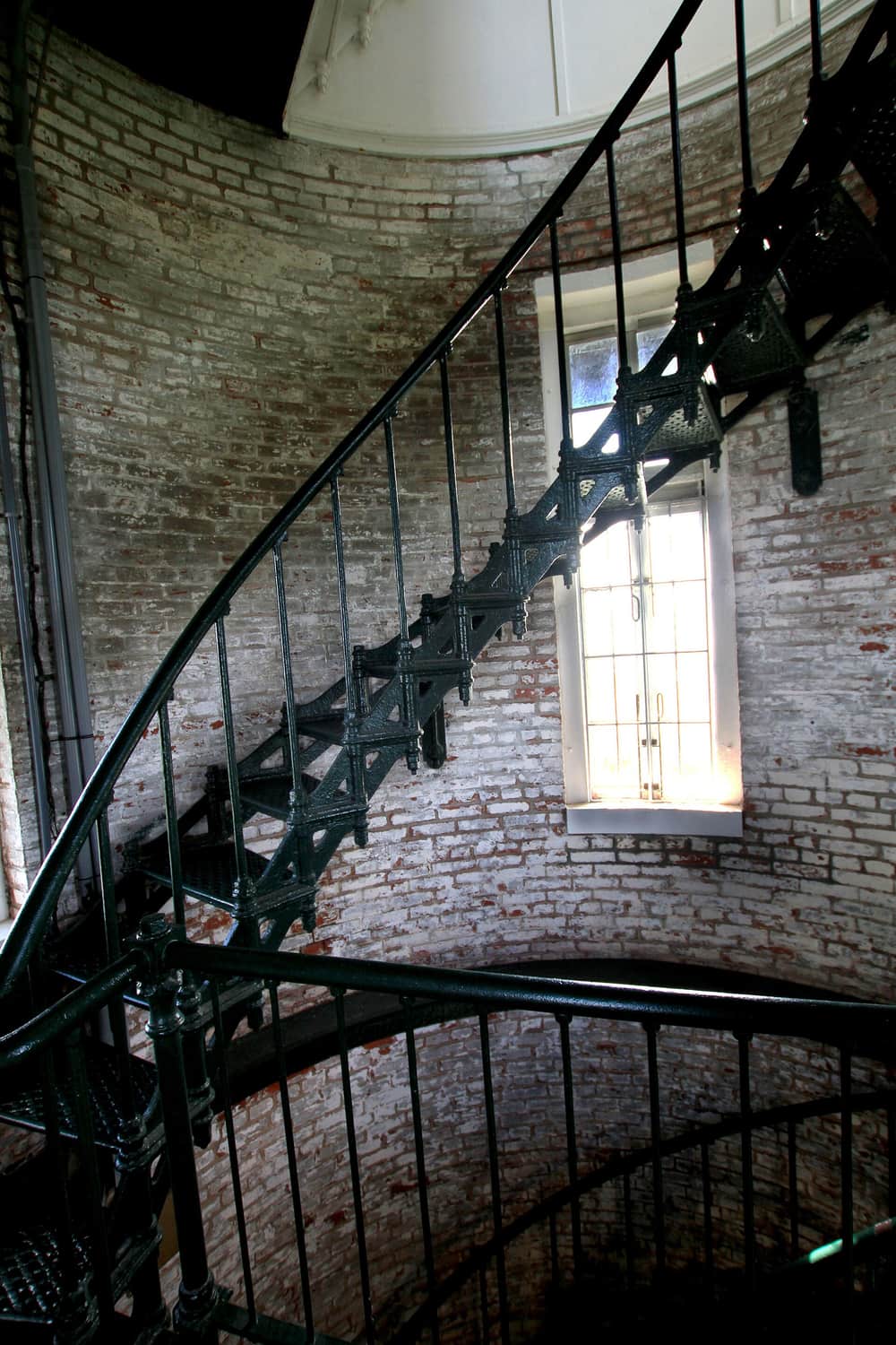 A tall window set deep into the brick wall of the stairwell, with the iron stairs beside it