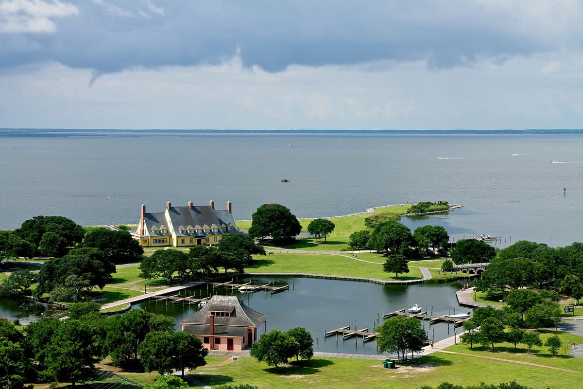 A large white house with green lawns on the edge of the sound, seen from above