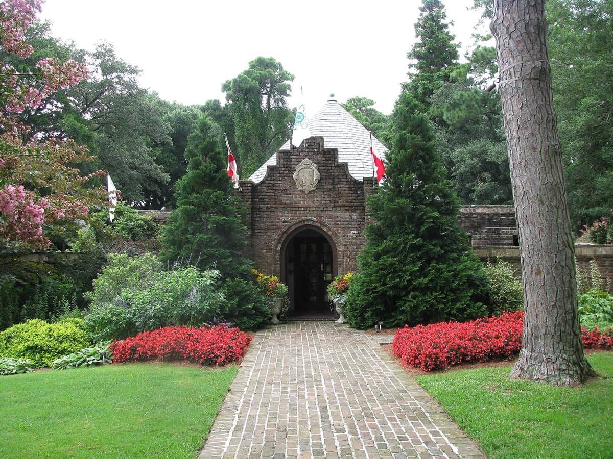 The brick gatehouse entrance to the Elizabethan Gardens with red flowers along the path