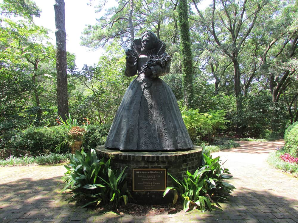 A bronze statue of Queen Elizabeth I standing on a plinth among trees at the Elizabethan Gardens