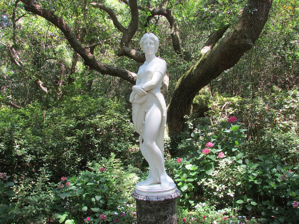 A white marble statue of Virginia Dare standing under live oaks at the Elizabethan Gardens