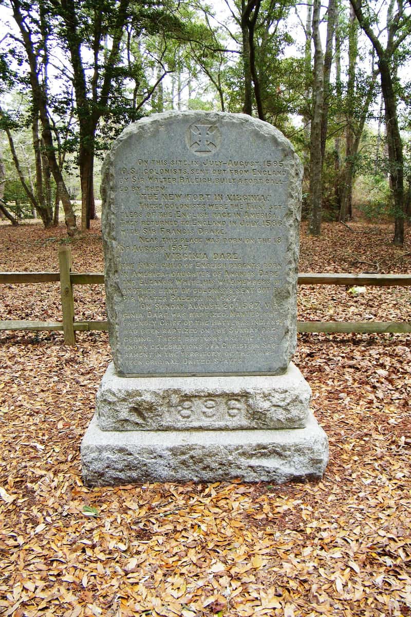 A stone monument to Virginia Dare standing among trees and fallen leaves at Fort Raleigh