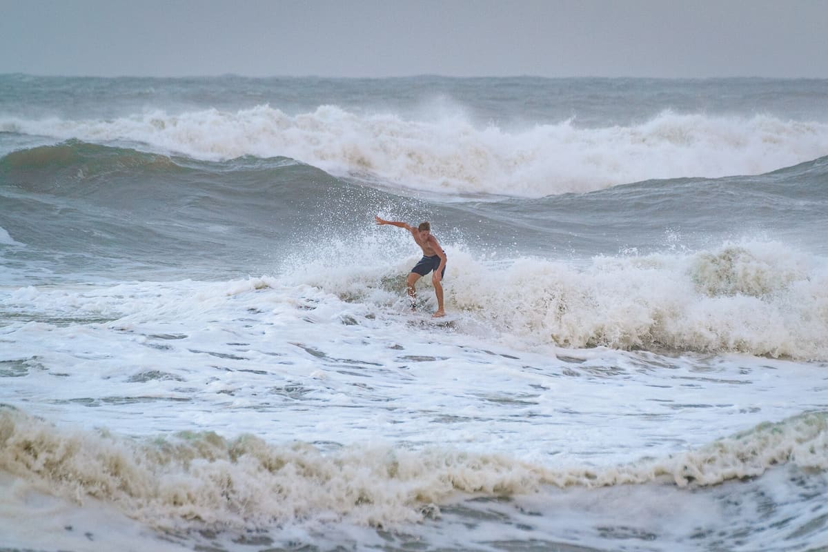 A surfer riding a wave in the broken water beside the pier