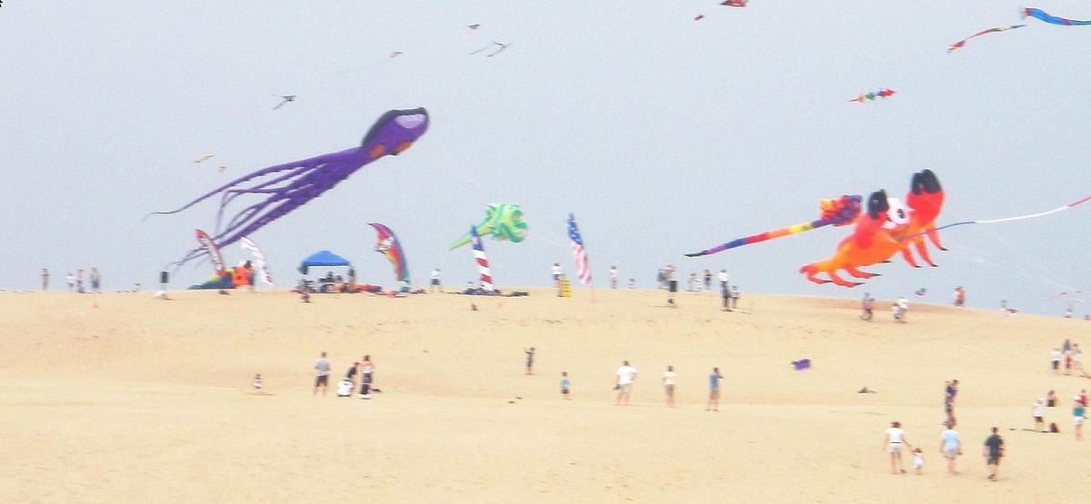 Large novelty kites shaped like an octopus and a crab flying above people on the dune