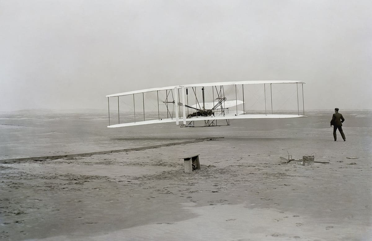 The 1903 Flyer just off the ground with Wilbur running at the wingtip